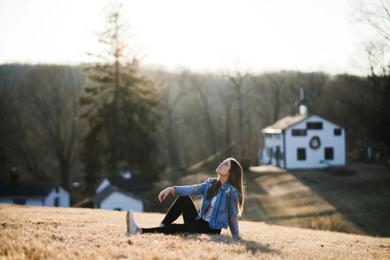 a girl sitting in the grass looking up at a white house