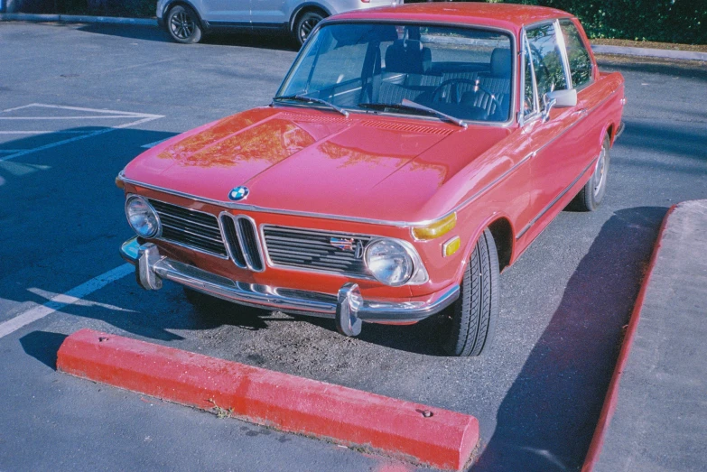 red car in parking lot, next to curb with fence