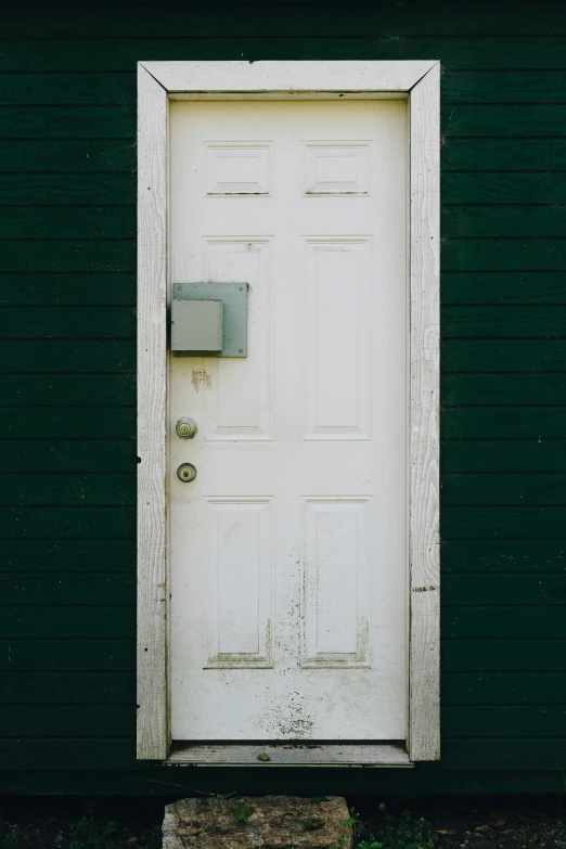 an empty white door is in front of a green building