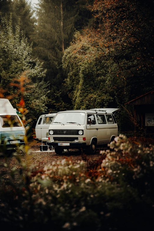 van, truck and camper parked on dirt near trees