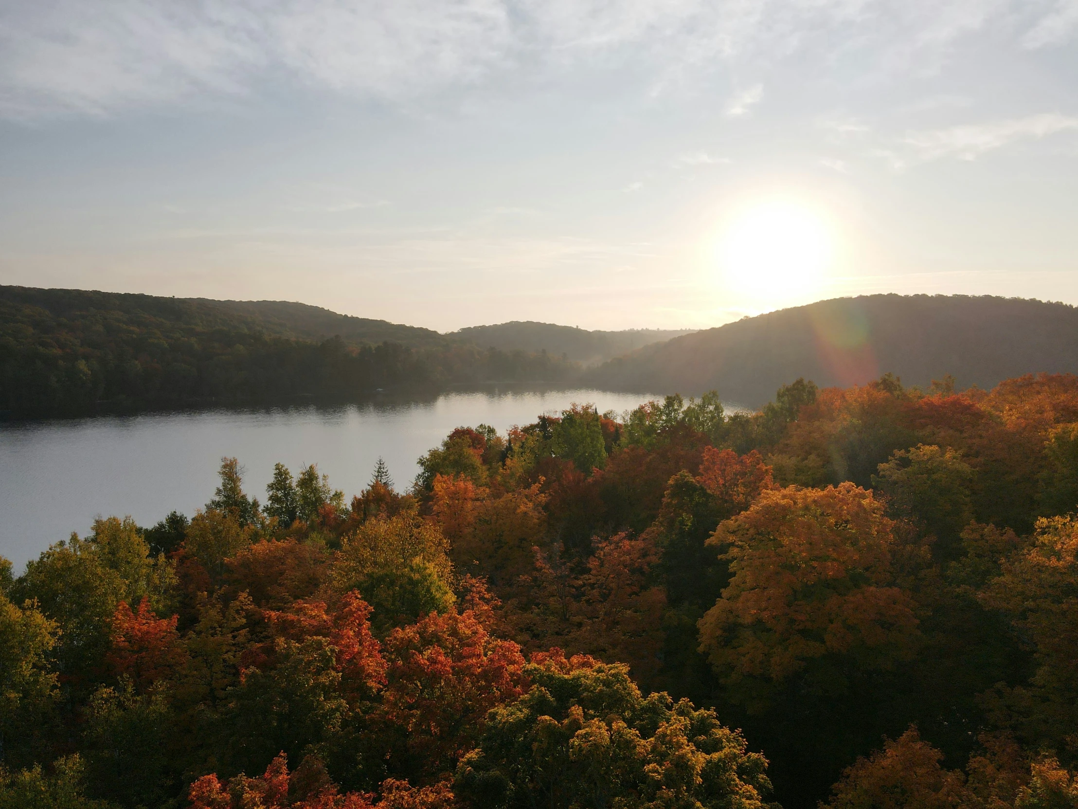 the sun is rising over trees in front of a body of water