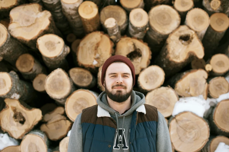 a man stands next to an enormous pile of logs