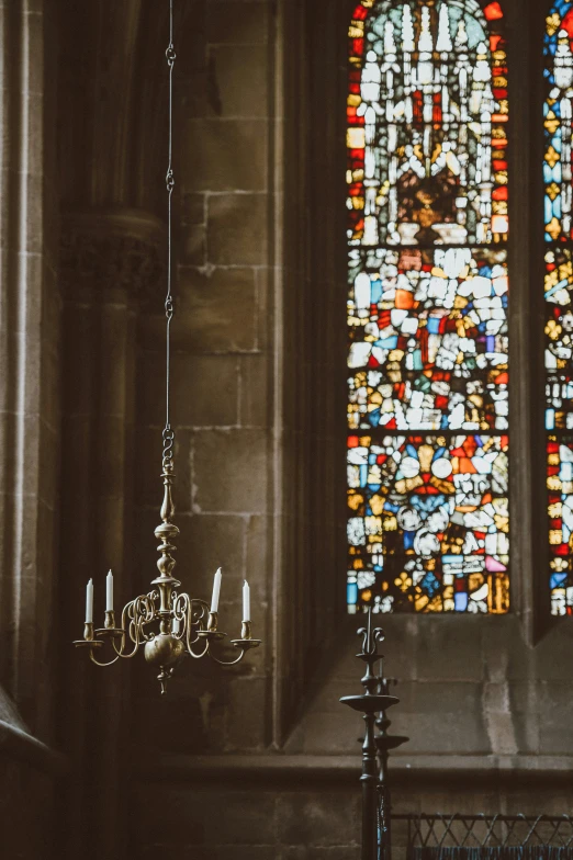 candles are hanging from a chandelier in front of an elaborate stained glass window