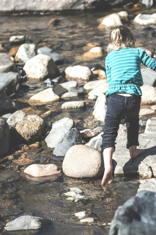 child playing with stones in water near large rocks