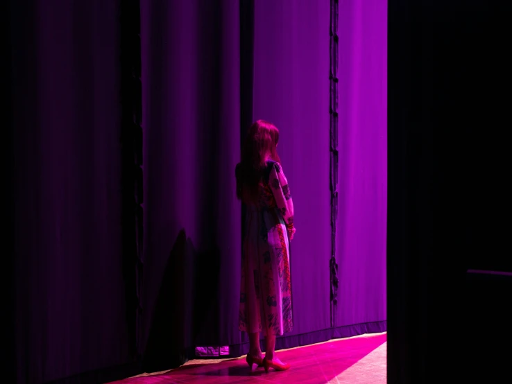 there is a woman standing alone in front of purple curtains