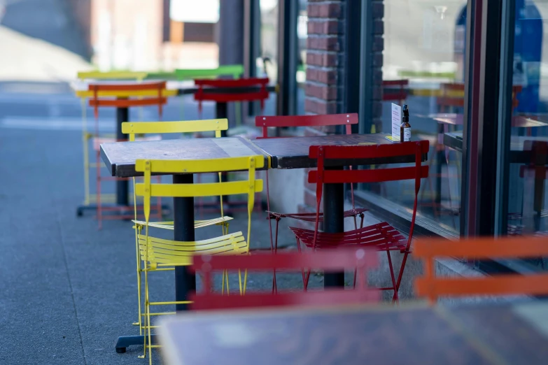 four tables with yellow, red and blue chairs in front of a building