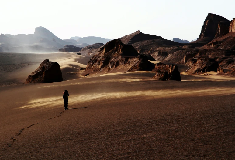 a man standing in the middle of a desert near big mountains