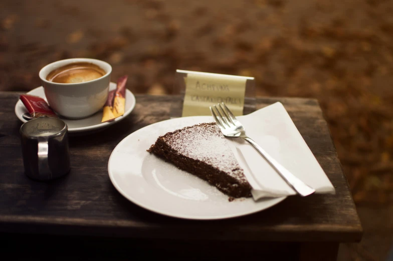 a small piece of chocolate cake on a white plate next to a cup of coffee