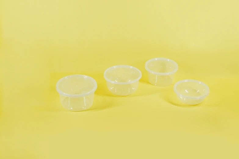 four small clear containers on yellow background with one empty and two without