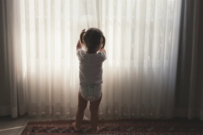 a little girl standing on a rug in front of the window