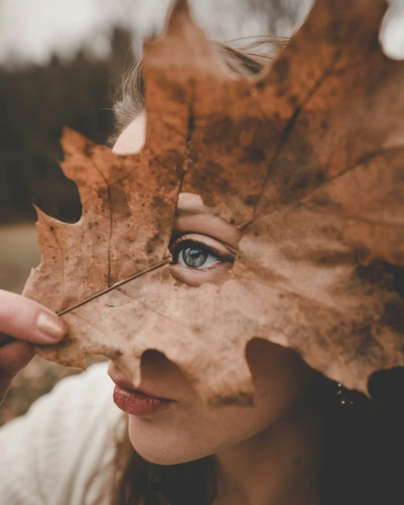 a young woman is holding a leaf above her head