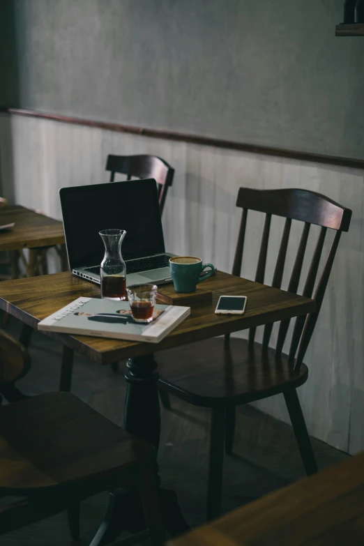 a laptop, glass pitcher, coffee cup and cellphone sitting on a table