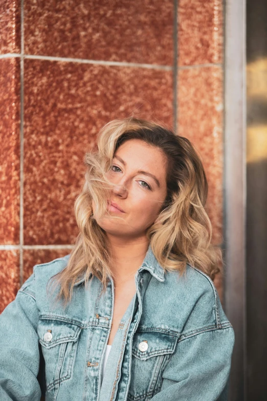 the woman is wearing a jean jacket in front of a wall