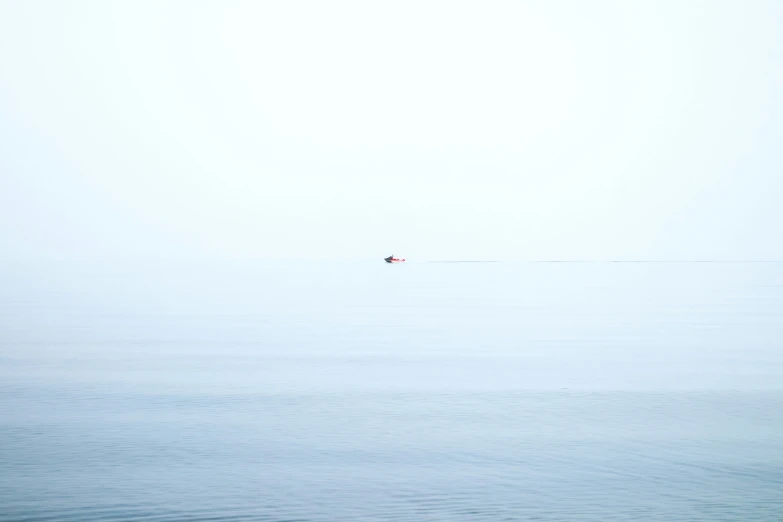 a single boat floating on the ocean on a hazy day