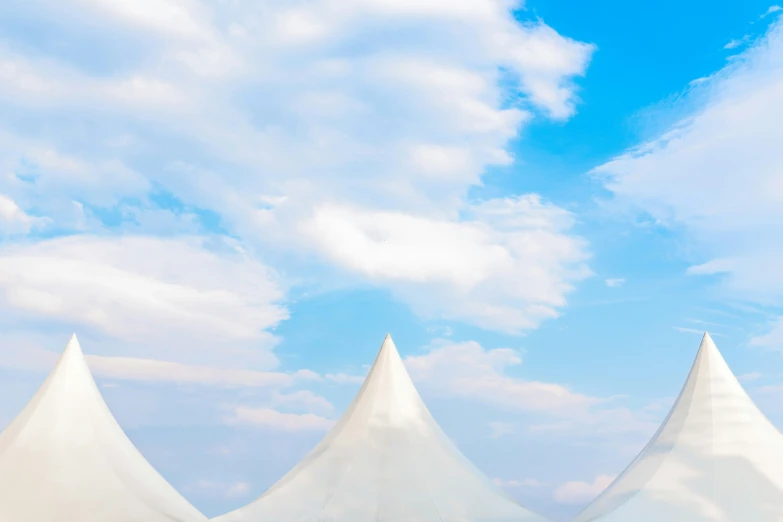 three white tents sitting on top of a field under a blue sky