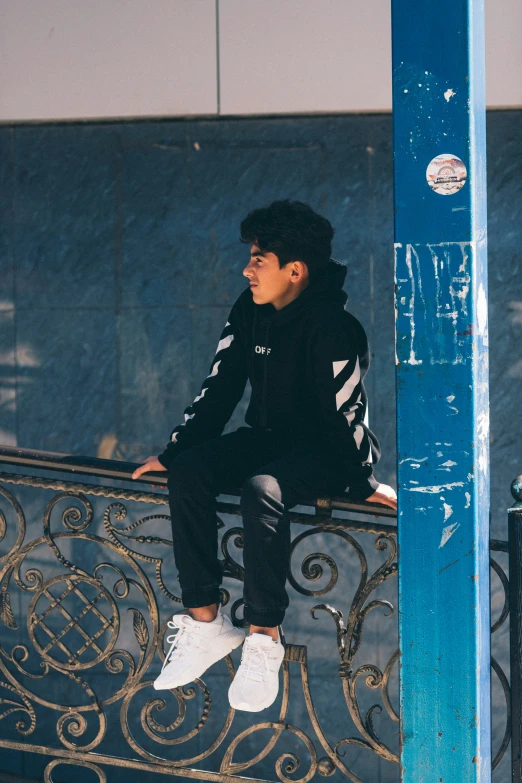 a man sitting on the top of a fence and wearing black clothes