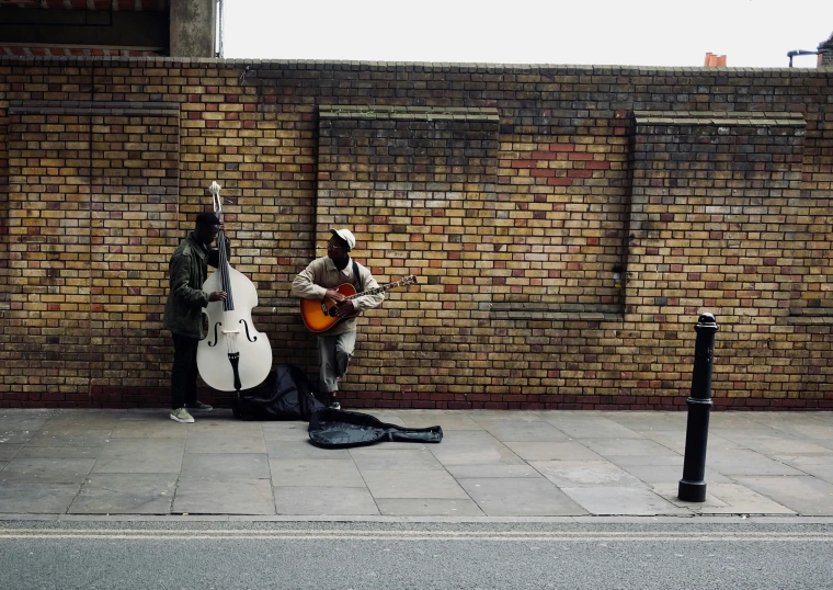 two musicians are playing near a brick wall