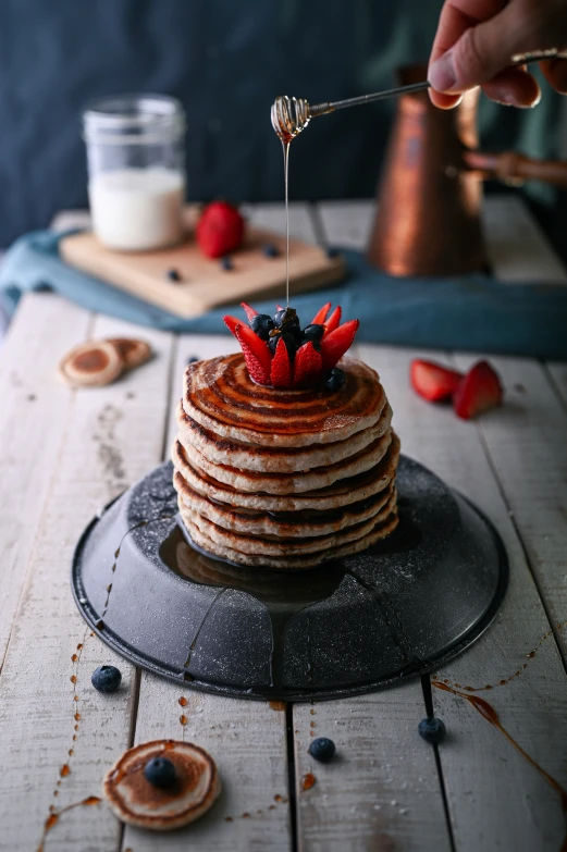 someone pouring syrup onto a stack of pancakes