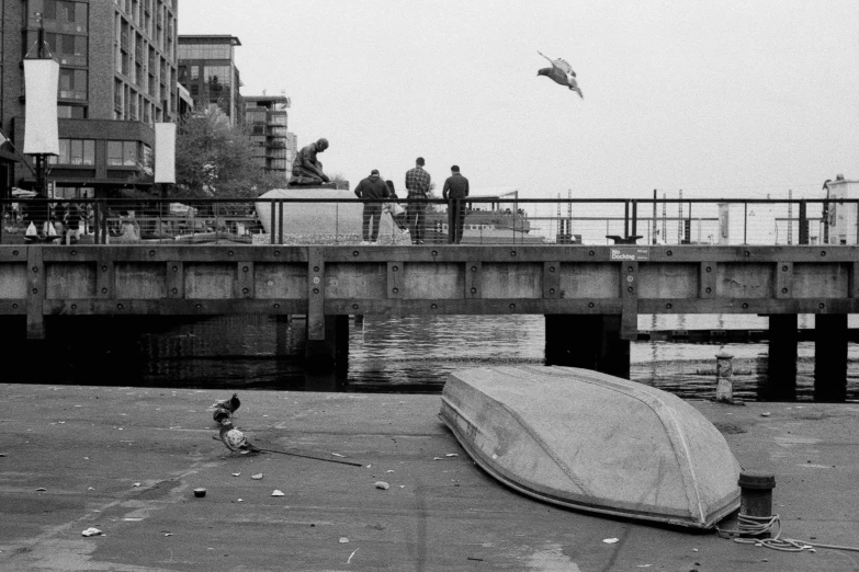 a boat lays on the ground and people stand on a dock near it