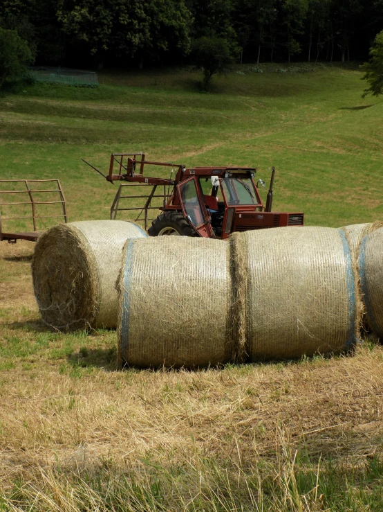 two hay bales are parked in the field as a tractor drives by