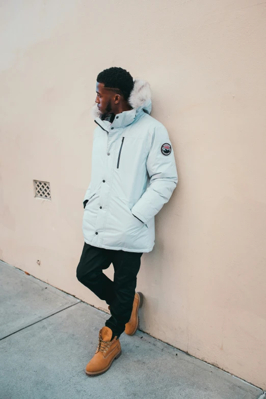 a man leaning against the wall wearing a hooded coat