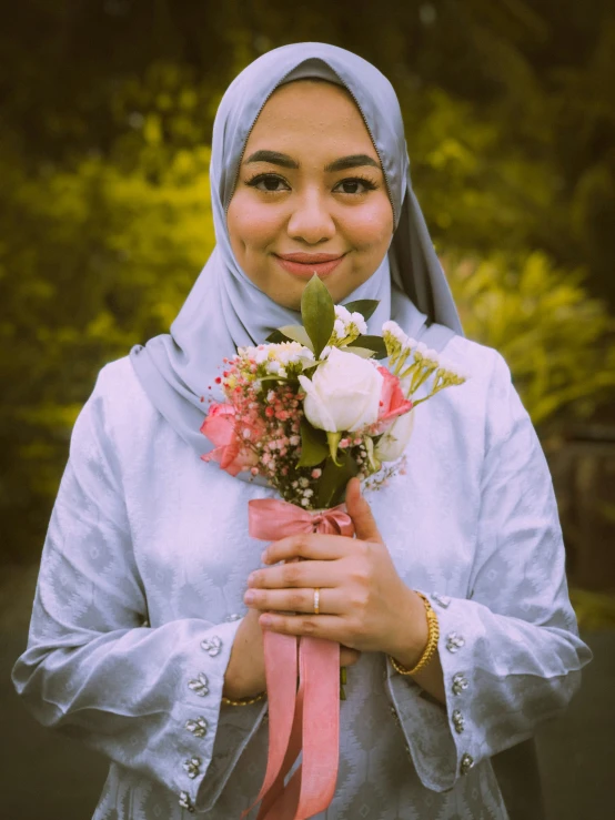 a woman in hijab is holding a bouquet of flowers