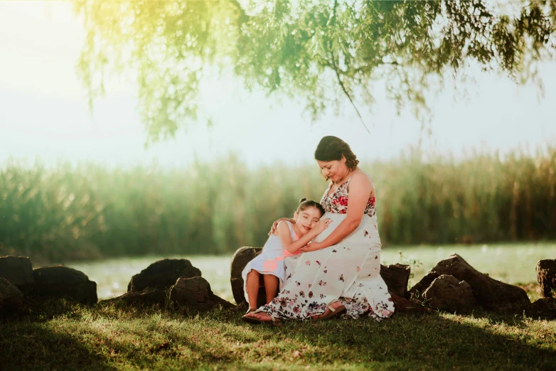 a woman and her child sitting on the grass under a tree