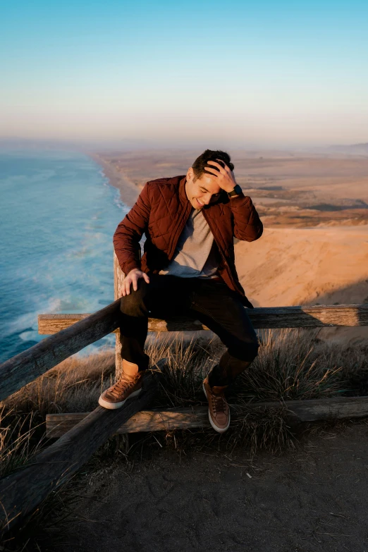 man in a jacket sitting on a bench at the edge of a cliff