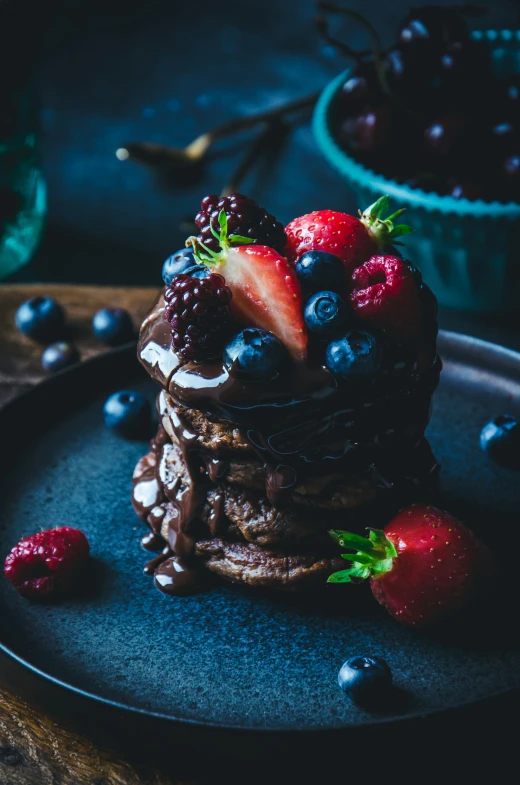 stack of pancakes with berries and chocolate syrup on a black plate