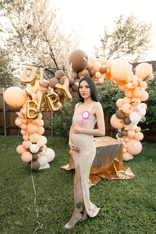 a pregnant woman posing next to balloons on the grass