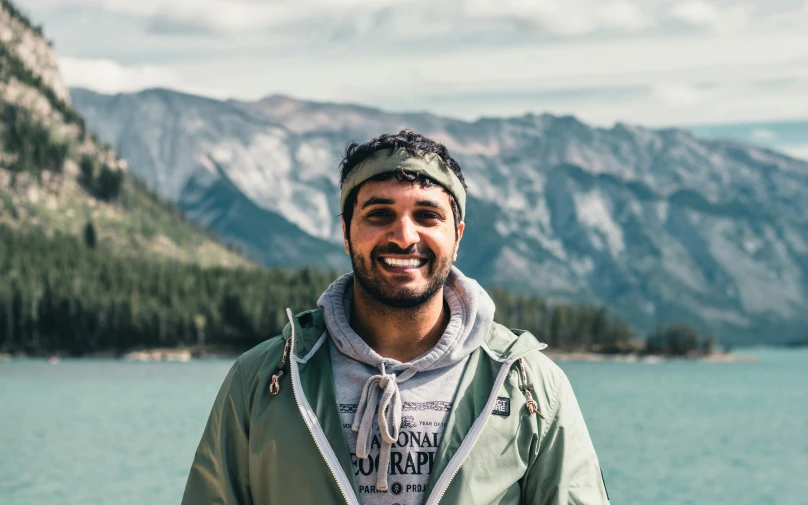 a man is standing by the water with mountains in the background