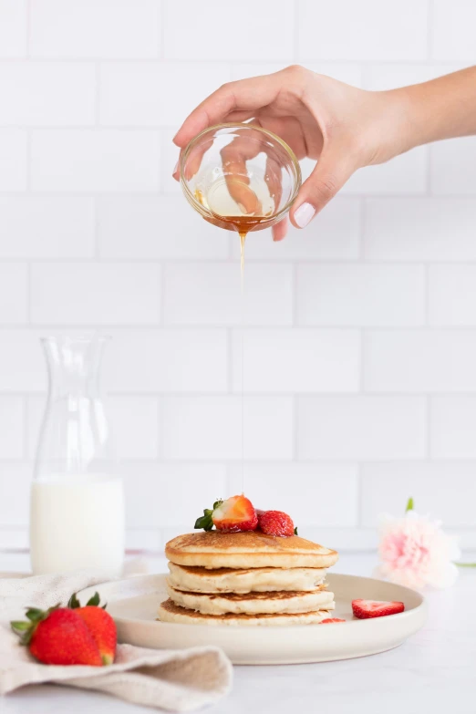 a person pouring syrup over some pancakes on a white plate