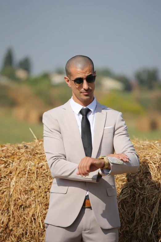 man in suit, tie and sunglasses leaning against hay bales
