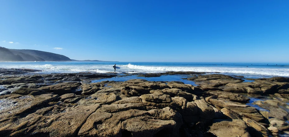 surfer walking on rocks towards the shore and water