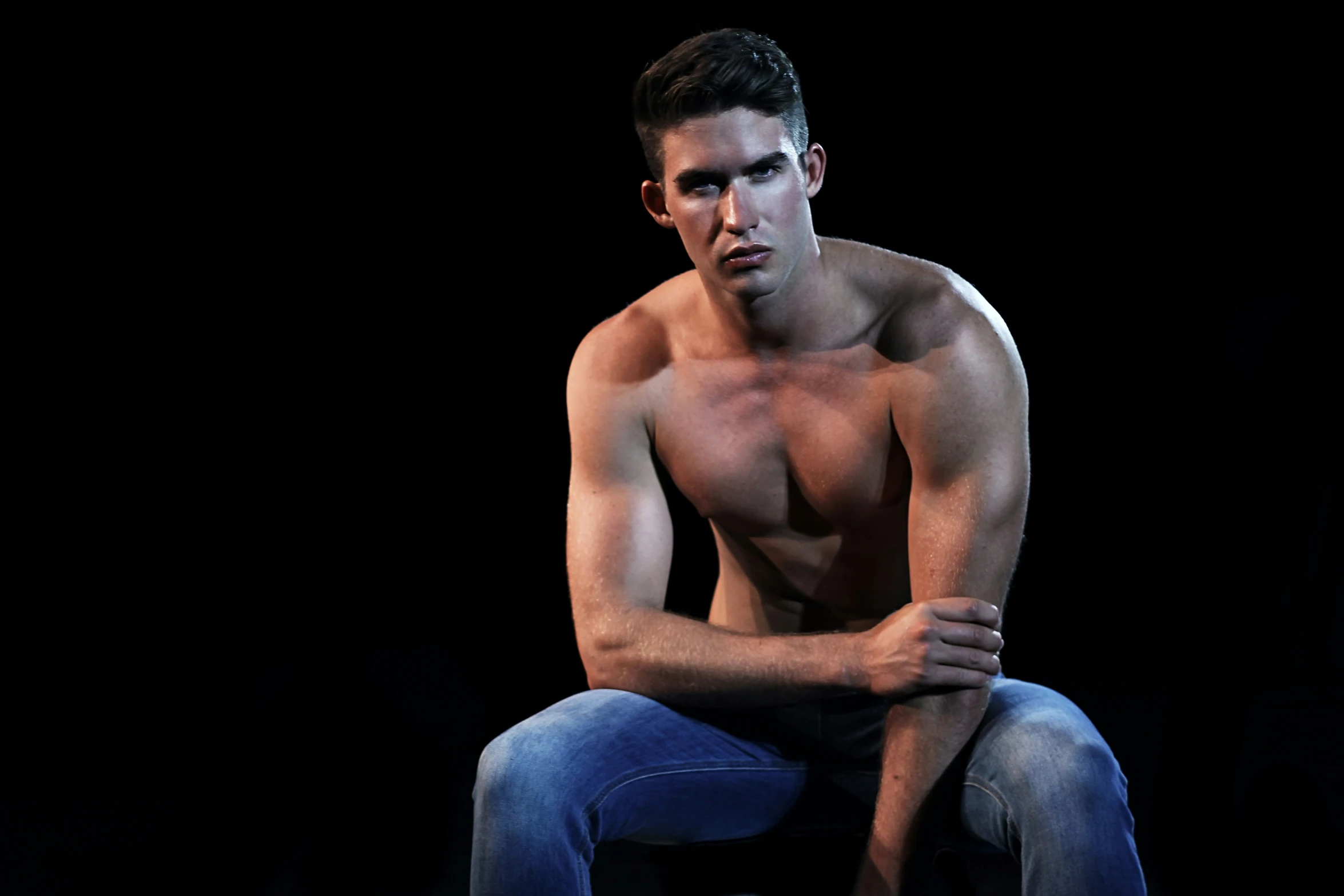 young man sitting shirtless in the spotlight