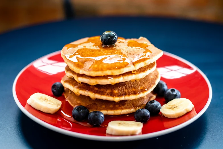 a stack of pancakes with blueberries and bananas on a red plate