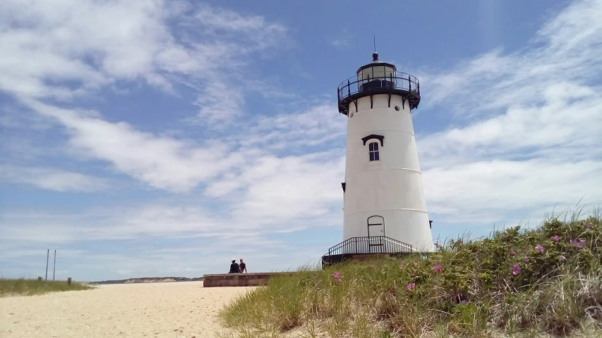 people stand on the grass beside the lighthouse