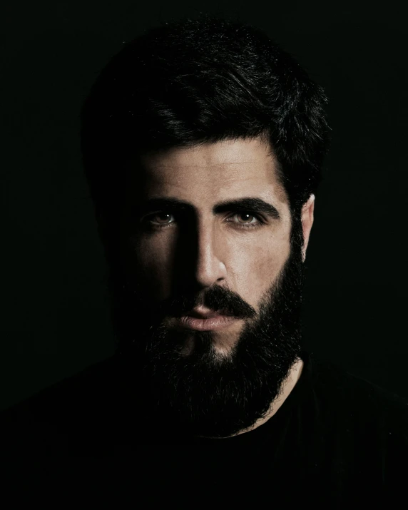 a man with dark hair and beard standing in a dark room