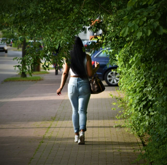 the back of a woman walking down a sidewalk past trees