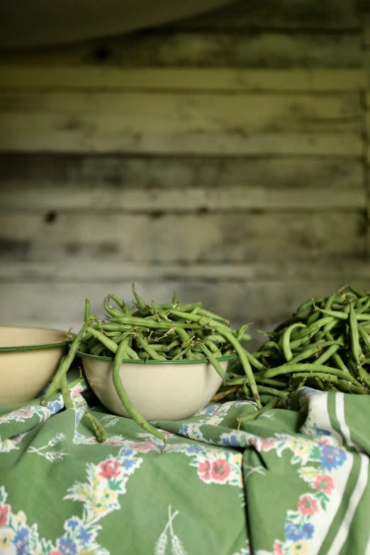 three white bowls filled with green beans next to some wood