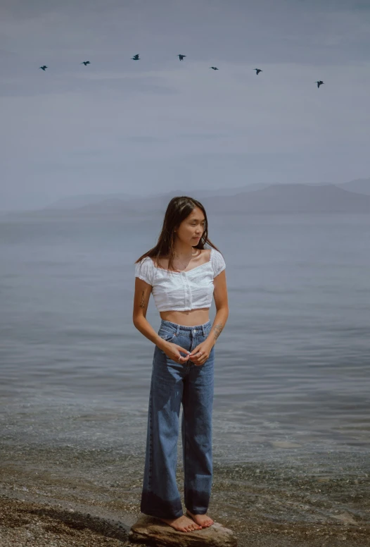 the young woman is standing on the beach with her arms raised