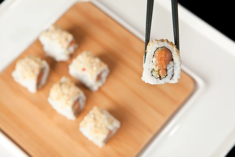 sushi being held up by chopsticks over a chopping board