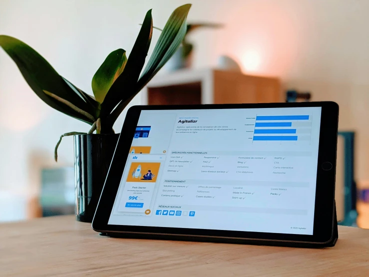 an ipad sits in front of a computer screen, with a potted plant