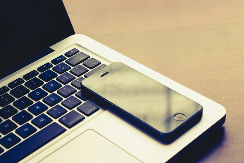 a cell phone that is laying on the keyboard of a laptop