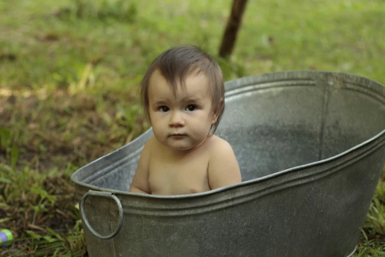 a little baby sits in a metal tub on grass