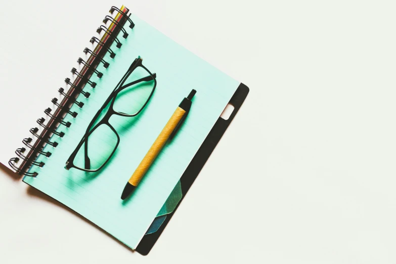 a notebook with a pencil, glasses, and pencil holder
