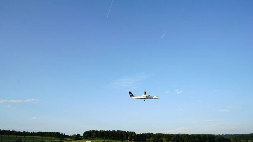 a airplane flying over a green field under a blue sky