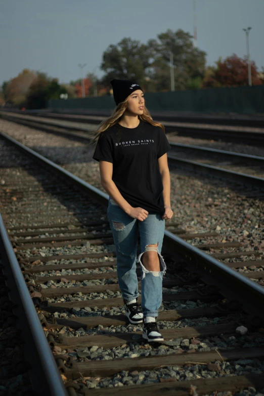 a teenaged girl with a black hat standing on a train track