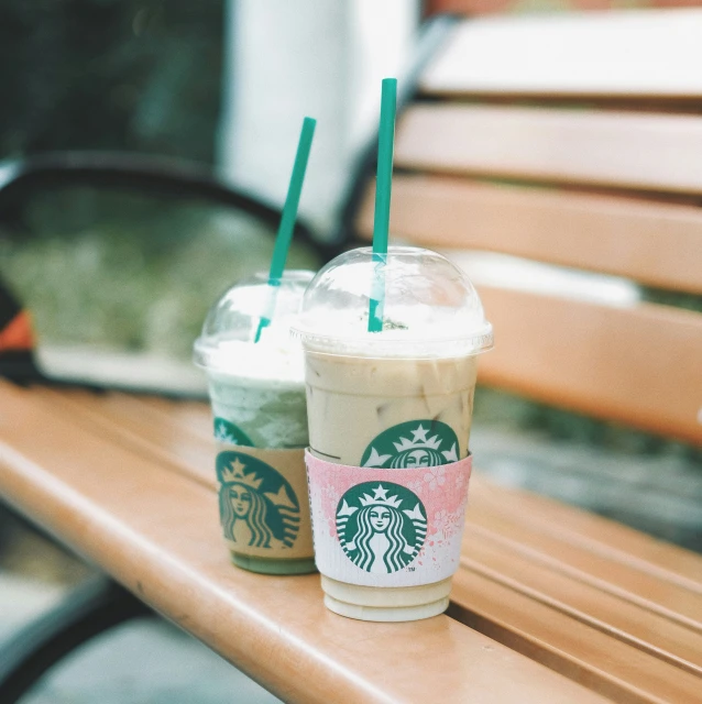 starbucks coffee drinks are sitting on a park bench