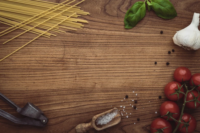 a bunch of spaghetti, tomatoes and garlic sitting on top of a wooden table